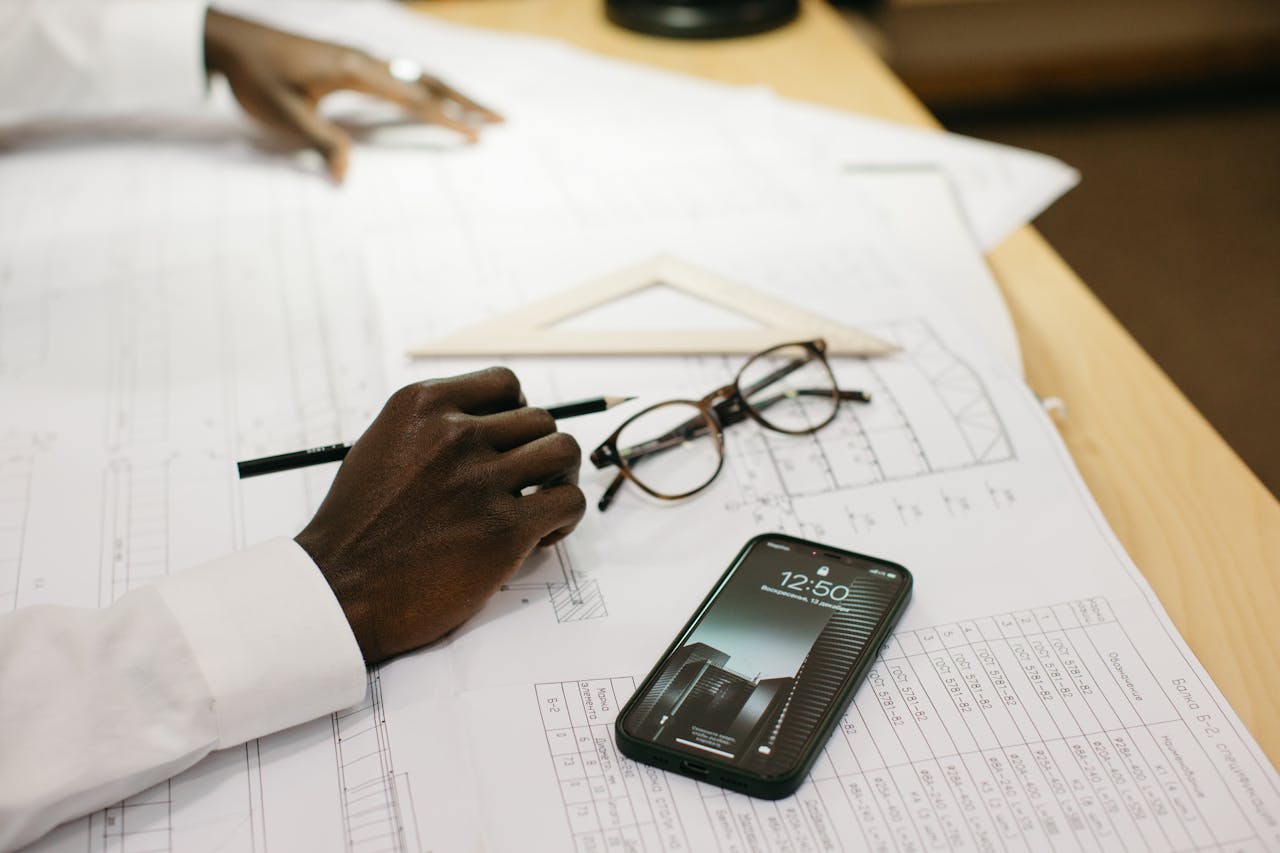 home-services-01 Close-up of an architect drafting on papers with a smartphone and glasses on a desk.